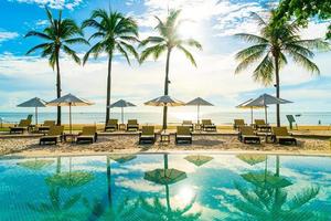 bellissimo ombrellone di lusso e sedia intorno alla piscina all'aperto in hotel e resort con palme da cocco su cielo blu foto