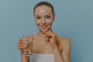 giovane donna attraente allegra con acqua potabile pulita e luminosa della pelle del viso per prevenire la disidratazione foto