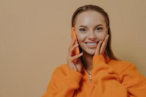 felice donna eccitata che parla al telefono, ascoltando buone notizie tramite telefono cellulare, isolata sopra il muro beige foto