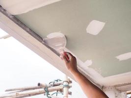 il soffitto lavoratore è intonacatura il soffitto articolazioni con alto qualità bianca gesso gesso per mantenere il articolazioni insieme. foto