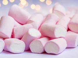 un' avvicinamento foto di un' gustoso rosa-bianco marshmallow con sfocata luci su un' sfondo