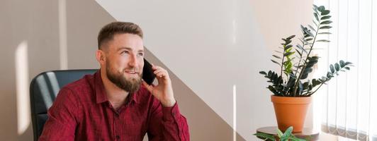 contento uomo d'affari a il suo scrivania nel ufficio parlando su Telefono. un' giovane uomo d'affari foto