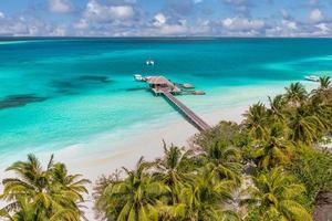 scenario paradisiaco delle maldive. paesaggio aereo tropicale, paesaggio marino con lungo molo, ville sull'acqua con splendida spiaggia di mare e laguna, natura tropicale. banner di destinazione turistica esotica, vacanze estive foto