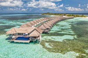 veduta aerea dell'isola delle maldive, resort di ville sull'acqua di lusso e molo in legno. bellissimo sfondo della spiaggia della laguna dell'oceano e del cielo. vacanze estive vacanze e concetto di viaggio. panorama del paesaggio aereo del paradiso foto