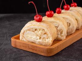 dolce meringa rotolo con fresco Pera, decorato con ciliegia su un' buio sfondo nel un' caffè negozio. foto