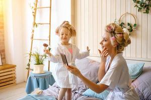 contento mamma e figlia rendere un' trucco seduta su il letto nel il Camera da letto foto