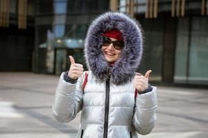 contento giovane donna nel inverno giacca con zaino vicino edificio foto