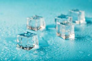 ghiaccio cubi siamo sparpagliato con acqua gocce sparpagliato su un' blu sfondo. vicino su. foto