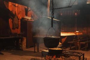 grande cucinando pentole siamo preparato utilizzando legna da ardere.metallo caldaie al di sopra di un' fuoco nel un' Casa con Fumo. foto