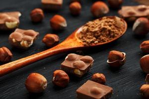 cioccolato con Nocciole e un' di legno cucchiaio con cacao su un' buio sfondo, circondato di noccioline nel il conchiglia e pelato. foto