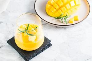 Mango frullato nel bicchieri e affettato Mango su un' piatto su il tavolo. fatti in casa dolce foto