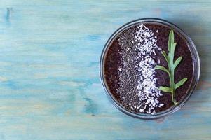 salutare vegano mirtillo frullato prima colazione con chia semi e Noce di cocco su un' blu di legno sfondo foto