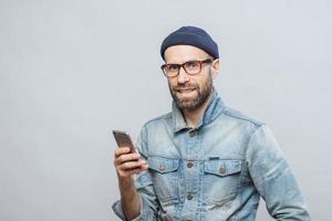 attraente modello maschile di mezza età con setole vestito con abiti alla moda, tiene smartphone, chatta con colleghi o amici in reti socail, isolato su sfondo bianco. tecnologia foto