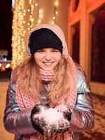 felice sorridente giovane donna caucasica in sciarpa, cappello, giacca, guanti durante la notte invernale all'aperto. anno nuovo, divertimento, concetto invernale foto