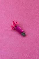 brillante rosa USB veloce memoria carta con un' rosa arco bugie su un' coperta di morbido e peloso leggero rosa vello tessuto. classico femmina regalo design per un' memoria carta foto