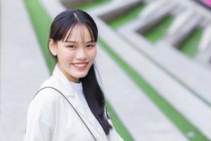 giovane donna di lavoro asiatica sicura di sé che indossa una camicia bianca e una borsa a tracolla sorride felicemente mentre è in piedi sulla strada per l'ufficio per lavoro in città. foto