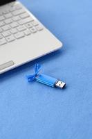 brillante blu USB veloce memoria carta con un' blu arco bugie su un' coperta di morbido e peloso leggero blu vello tessuto accanto per un' bianca il computer portatile. classico femmina regalo design per un' memoria carta foto