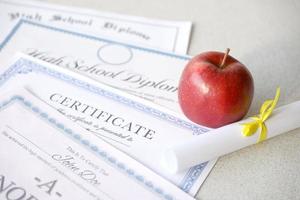 un' onore rotolo riconoscimento, certificato di realizzazione e alto scuola diploma bugie su tavolo con piccolo scorrere e rosso Mela. formazione scolastica documenti foto