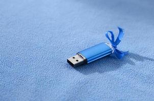 brillante blu USB veloce memoria carta con un' blu arco bugie su un' coperta di morbido e peloso leggero blu vello tessuto. classico femmina regalo design per un' memoria carta foto