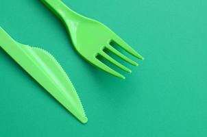 monouso plastica posate verde. plastica forchetta e coltello menzogna su un' verde sfondo superficie foto
