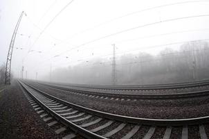 il ferrovia traccia nel un' nebbioso mattina. un' lotto di rotaie e traversine partire in il nebbioso orizzonte. fisheye foto con è aumentato distorsione