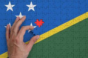 Salomone isole bandiera è raffigurato su un' puzzle, quale il dell'uomo mano completa per piegare foto