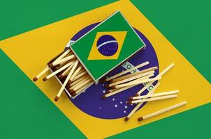 brasile bandiera è mostrato su un Aperto scatola di fiammiferi, a partire dal quale parecchi fiammiferi autunno e bugie su un' grande bandiera foto