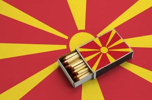 macedonia bandiera è mostrato nel un Aperto scatola di fiammiferi, quale è pieno con fiammiferi e bugie su un' grande bandiera foto