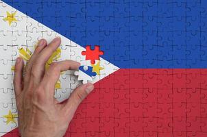 Filippine bandiera è raffigurato su un' puzzle, quale il dell'uomo mano completa per piegare foto