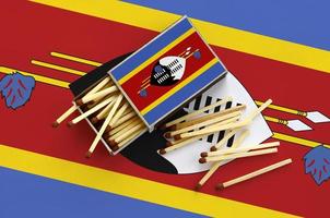 Swaziland bandiera è mostrato su un Aperto scatola di fiammiferi, a partire dal quale parecchi fiammiferi autunno e bugie su un' grande bandiera foto
