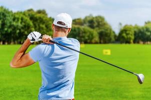 bene colpire. posteriore Visualizza di maschio giocatore giocando golf mentre in piedi su verde foto