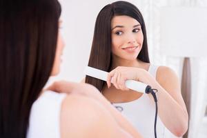 donna pettinatura capelli. attraente giovane donna pettinatura sua capelli mentre guardare a il specchio foto