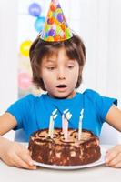 che cosa un' sorpresa sorpreso poco ragazzo guardare a il compleanno torta e preparazione per soffio il candele foto