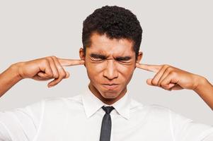 Questo è pure forte frustrato giovane afro americano uomo nel vestito formale tamponamento orecchie con il suo dita e conservazione occhi chiuso mentre in piedi contro grigio sfondo foto