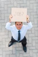 avuto lavoro superiore Visualizza di bello giovane uomo nel camicia e cravatta mostrando manifesto con lavoro testo Messaggio mentre in piedi all'aperto foto