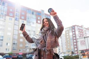 giovane riuscito soddisfatto con se stessa donna danza ascoltando per musica nel cuffie a partire dal mobile Telefono su città panorama foto