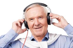 musica per tutti età. ritratto di anziano uomo nel cuffie ascoltando per musica e sorridente mentre in piedi contro bianca sfondo foto