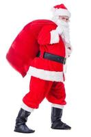 Santa Claus su il andare. pieno lunghezza di tradizionale Santa Claus trasporto sacco con regali e guardare a telecamera mentre a piedi contro bianca sfondo foto