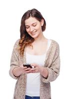 digitando Messaggio per amico. allegro giovane donna Tenere mobile Telefono e sorridente mentre in piedi isolato su bianca foto
