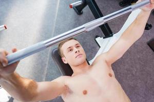 sollevamento pesi nel palestra. superiore Visualizza di fiducioso giovane muscolare uomo Lavorando su su panchina stampa foto