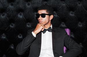 individuale stile. alla moda giovane afro americano uomo seduta su il sedia Tenere mano su mento foto