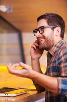 bene parlare con amico. bello giovane uomo parlando su il mobile Telefono e sorridente mentre seduta nel bar foto