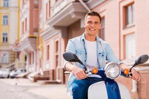 la libertà per partire ovunque. bello giovane uomo equitazione scooter lungo il strada e sorridente foto