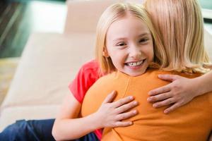 sensazione così contento vicino mamma. contento madre e figlia abbracciare mentre seduta su il divano insieme foto