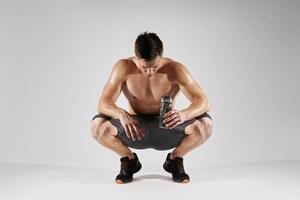 stanco muscolare uomo Tenere bottiglia con acqua contro bianca sfondo foto