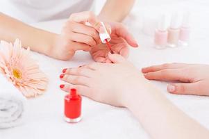 manicure nel azione. avvicinamento di manicure fare rosso manicure per femmina cliente foto