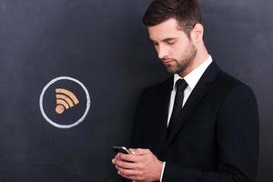 Wi-Fi zona. bello giovane uomo Tenere telefono mentre in piedi contro condivisione simbolo gesso disegno su lavagna foto