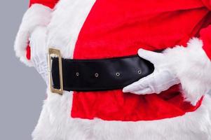 Santa è Qui avvicinamento lato Visualizza di tradizionale Santa Claus regolazione il suo cintura mentre in piedi contro grigio sfondo foto