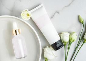 cosmetici impostato di rosa bellezza viso olio nel contagocce bottiglia e senza marchio tubo con crema o maschera su marmo tavolo con eustoma fiori. di moda piatto posare stillife foto