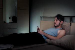 giovane uomo utilizzando mobile Telefono su il letto a notte. foto